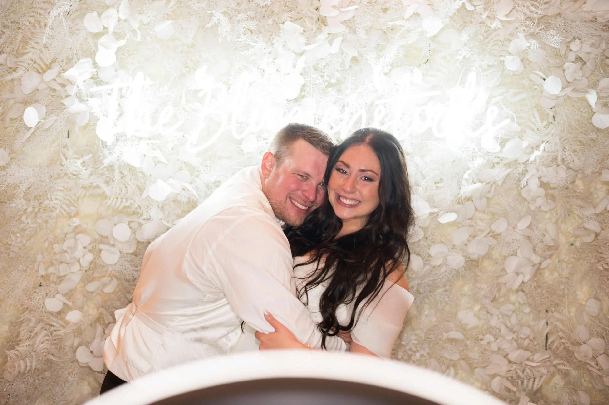 Couple laughing together in photo booth with cream and white floral backdrop