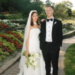 Bride in strapless gown with veil and groom in black tuxedo standing on brick pathway surrounded by terraced gardens