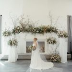 Bride with cathedral veil standing before elaborate ceremony arch decorated with organic florals and branches