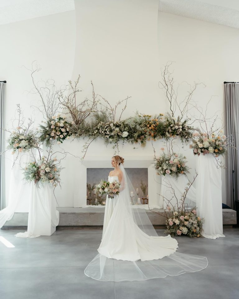 Bride with cathedral veil standing before elaborate ceremony arch decorated with organic florals and branches
