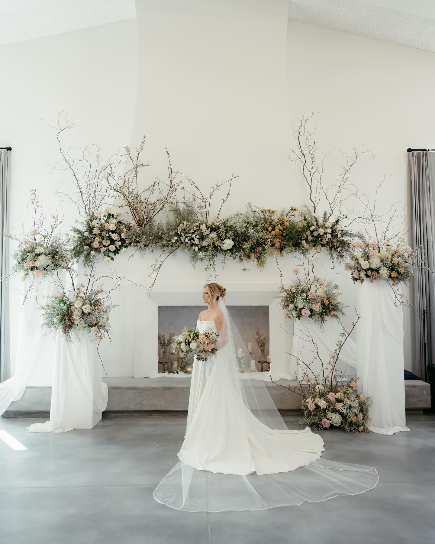 Bride with cathedral veil standing before elaborate ceremony arch decorated with organic florals and branches
