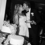 Bride and groom kissing while cutting their white wedding cake decorated with baby's breath flowers