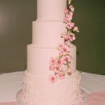 Four-tier blush pink wedding cake with delicate lace piping and cascading pink cherry blossoms