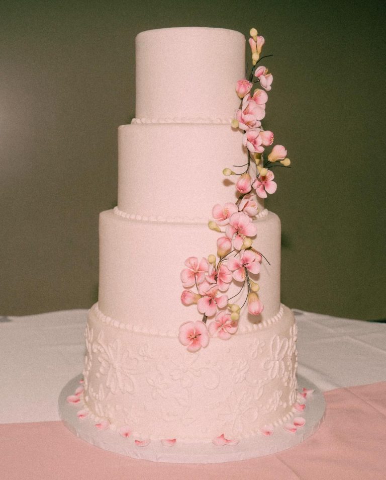Four-tier blush pink wedding cake with delicate lace piping and cascading pink cherry blossoms