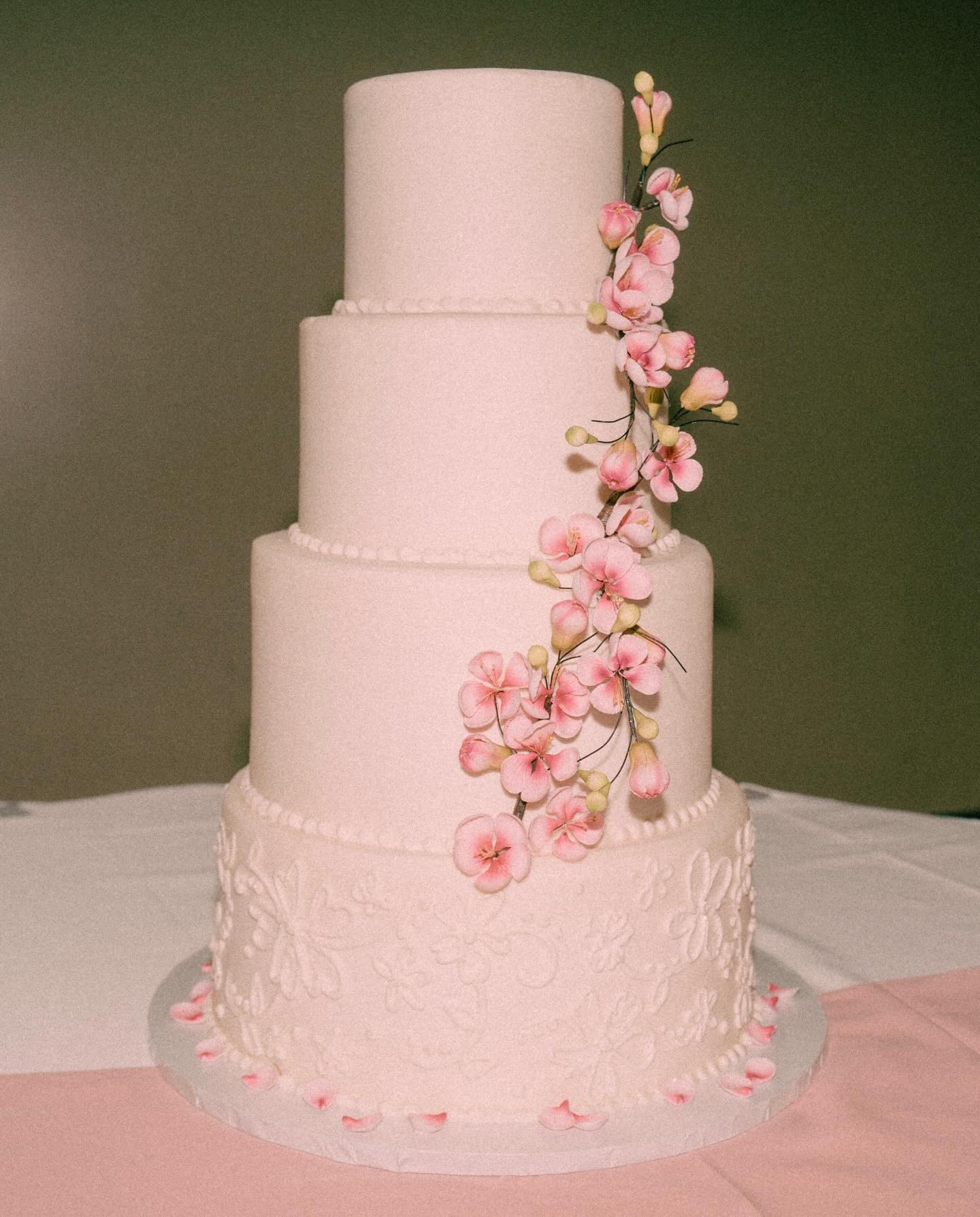 Four-tier blush pink wedding cake with delicate lace piping and cascading pink cherry blossoms