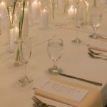 Elegant white table setting with candles, flowers, and place settings for wedding reception