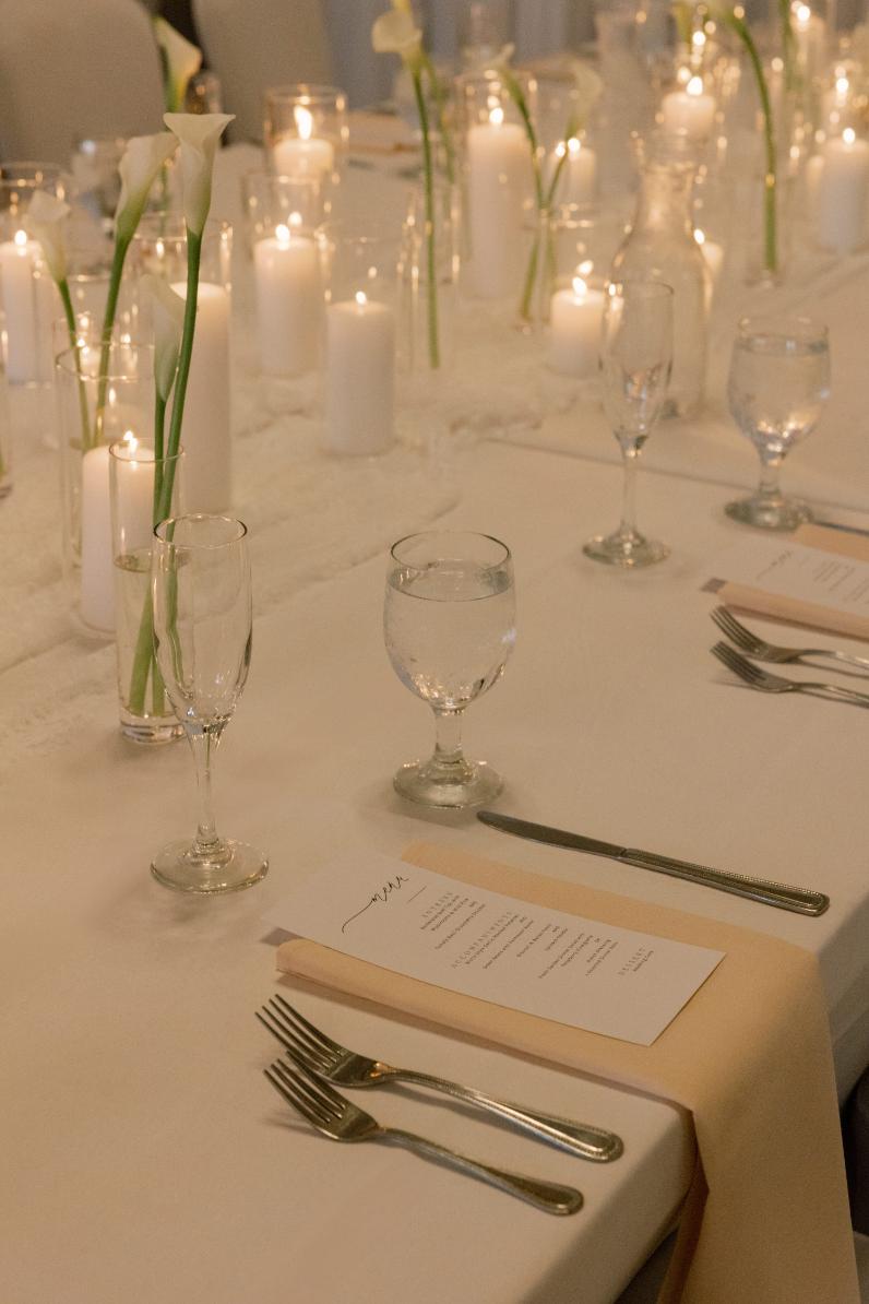 Elegant white table setting with candles, flowers, and place settings for wedding reception