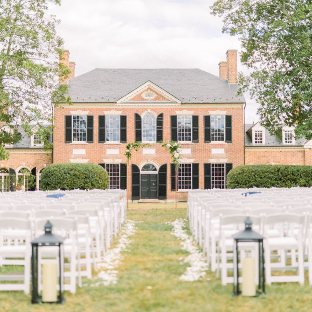 Historic brick mansion with outdoor ceremony setup featuring white folding chairs and lanterns on lawn