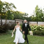 Bride and groom walking together in garden setting at outdoor wedding reception