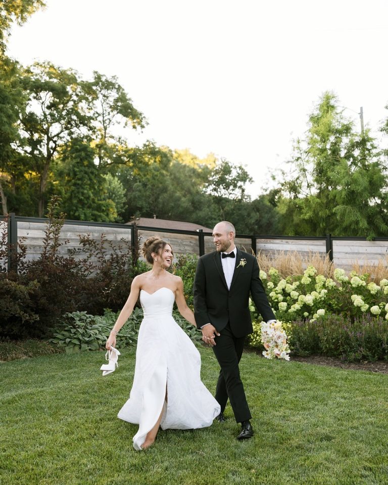 Bride and groom walking together in garden setting at outdoor wedding reception