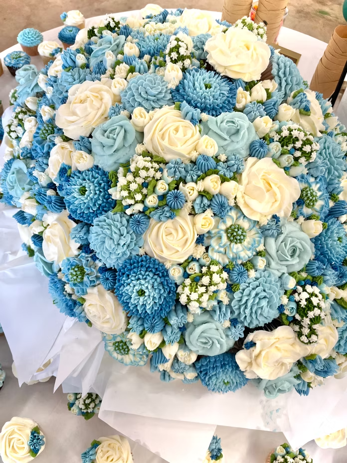 Wedding cupcake arrangement featuring buttercream flowers in blue and ivory creating a floral bouquet design