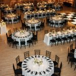 Wedding reception hall with white-clothed round tables, black chairs, candlelight, and illuminated geometric wall panels