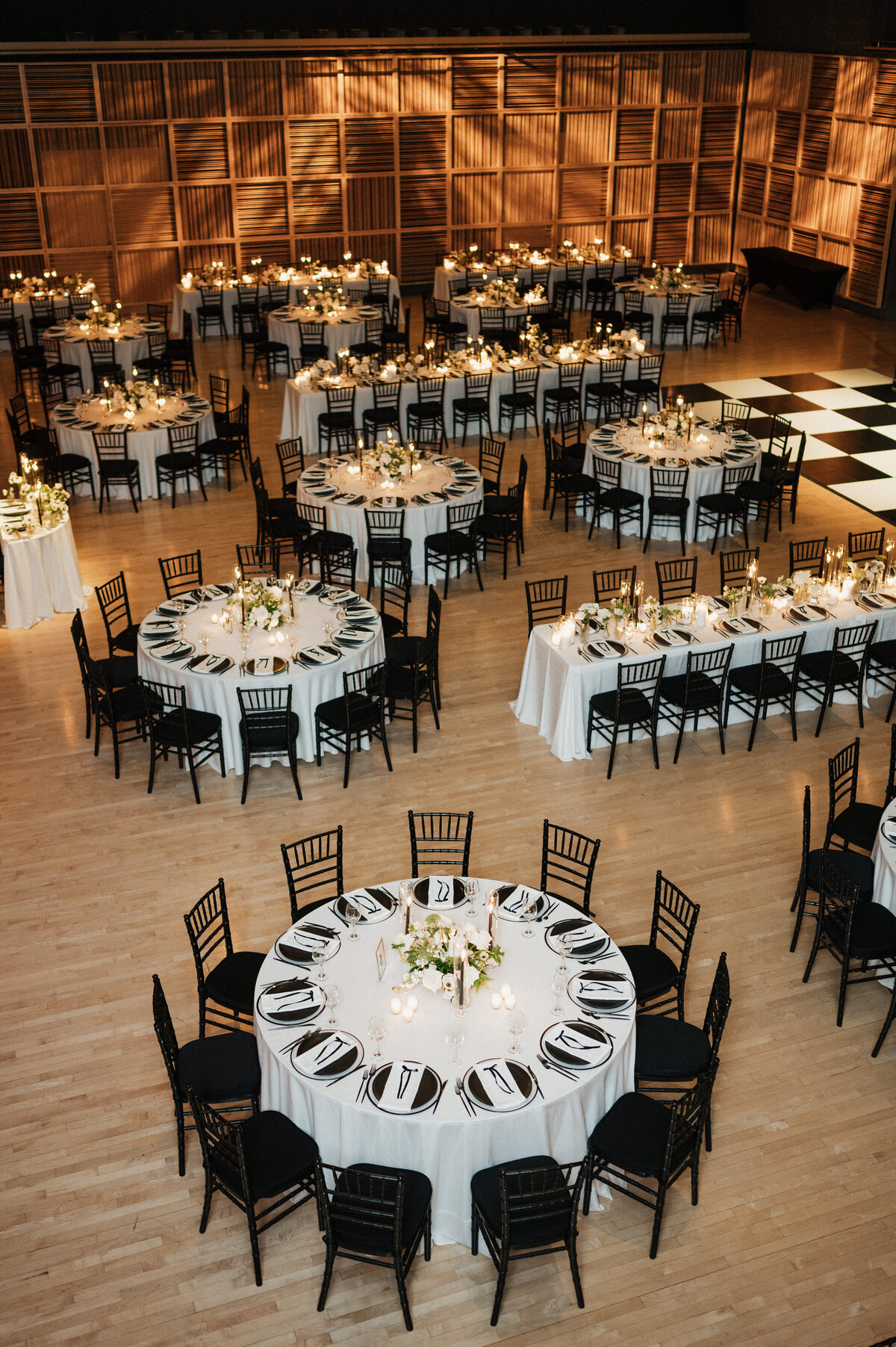 Wedding reception hall with white-clothed round tables, black chairs, candlelight, and illuminated geometric wall panels