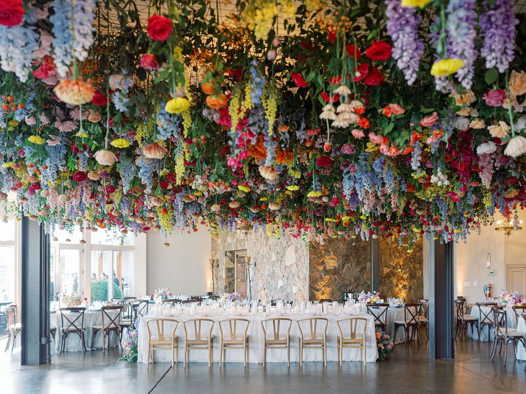 Elegant reception hall with dramatic hanging floral installation featuring colorful blooms suspended from ceiling