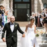 Newlyweds exit historic stone building during ribbon wand send-off with wedding party celebrating around them
