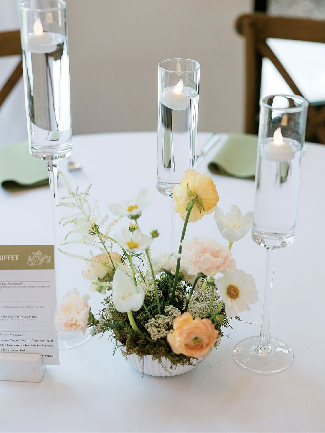 Elegant wedding table centerpiece featuring pastel florals with moss base and tall floating candles