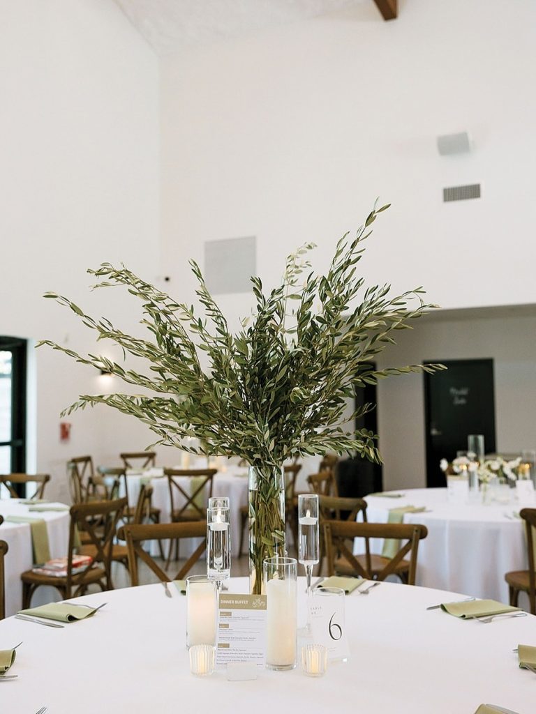 Modern wedding table setting with tall greenery centerpiece, candles, and table number six