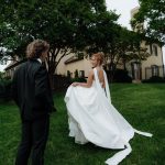 Bride in minimalist halter neck gown with open back and flowing cape detail outdoors with groom