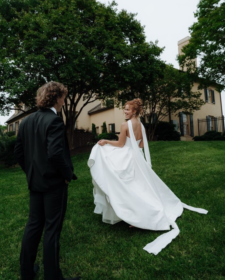 Bride in minimalist halter neck gown with open back and flowing cape detail outdoors with groom