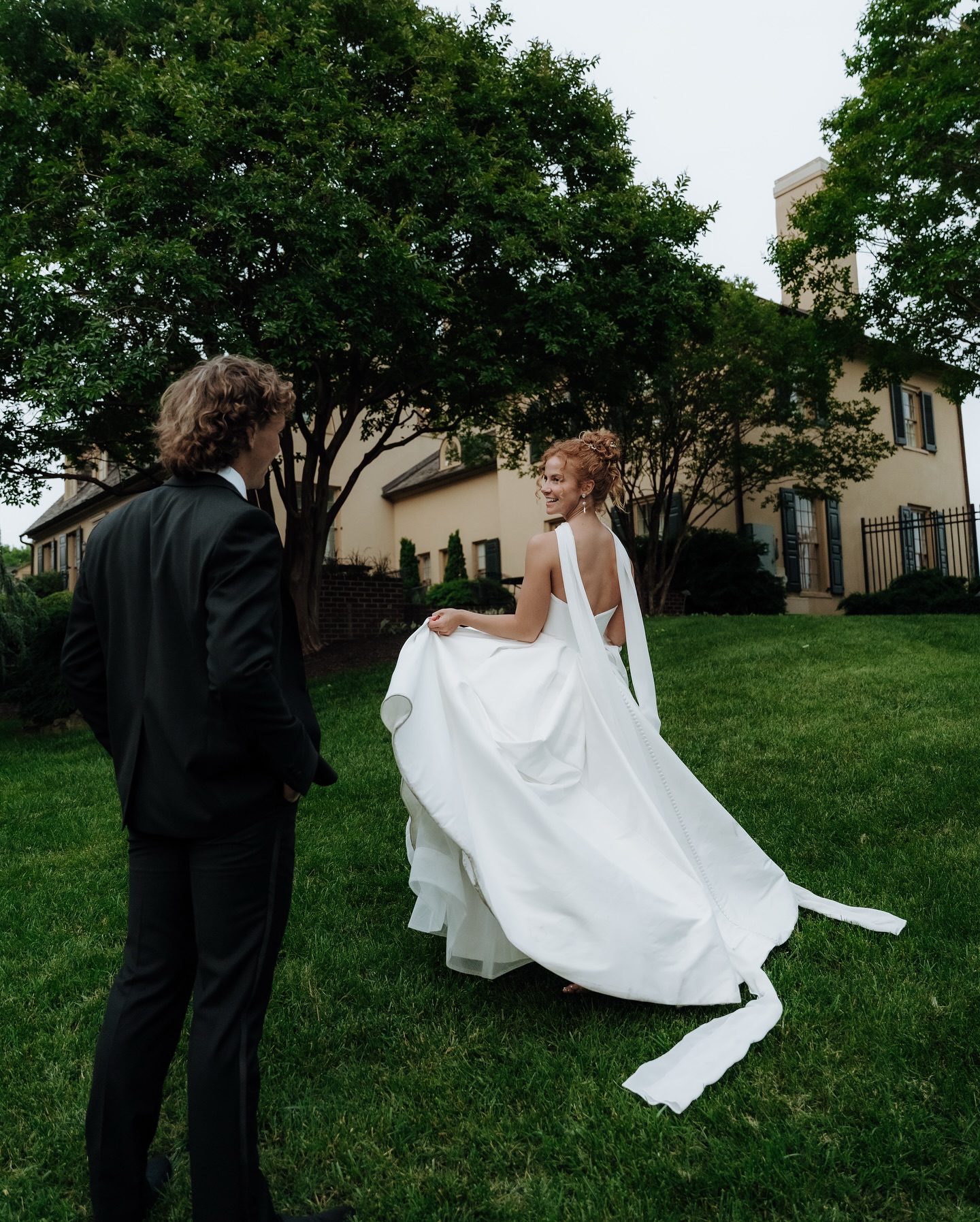 Bride in minimalist halter neck gown with open back and flowing cape detail outdoors with groom