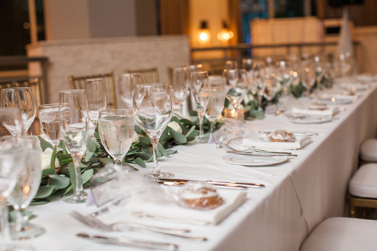 Close-up of formal dining table with eucalyptus garland running down the center and multiple wine glasses at each setting