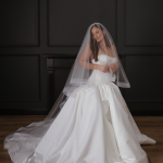 Bride in strapless ball gown with cathedral veil and flowing train against dark wall