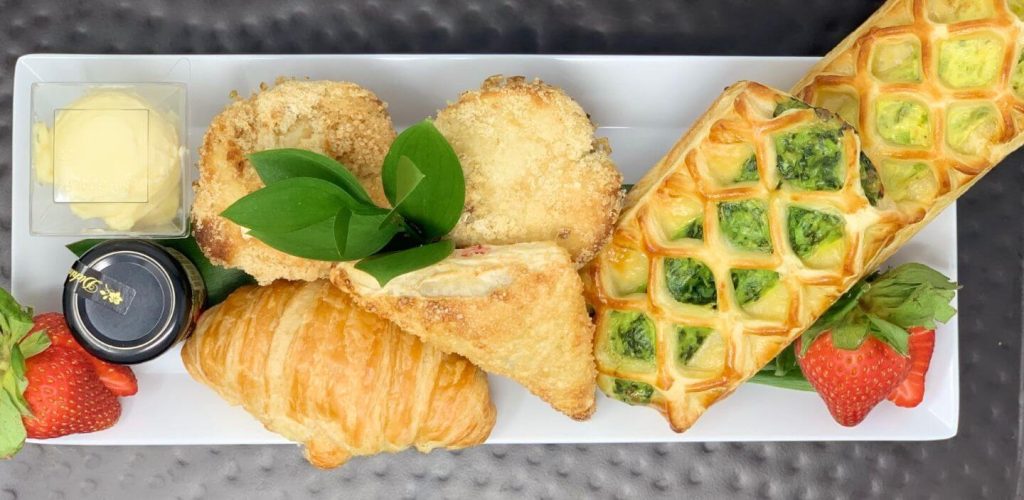 Sophisticated brunch platter with breaded chicken, green waffle, flaky croissant, butter, and strawberries
