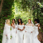 Five brides in elegant white wedding gowns standing under a lush green ivy archway in Marietta