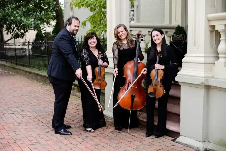 String quartet in formal black attire posing with violins and cello outdoors