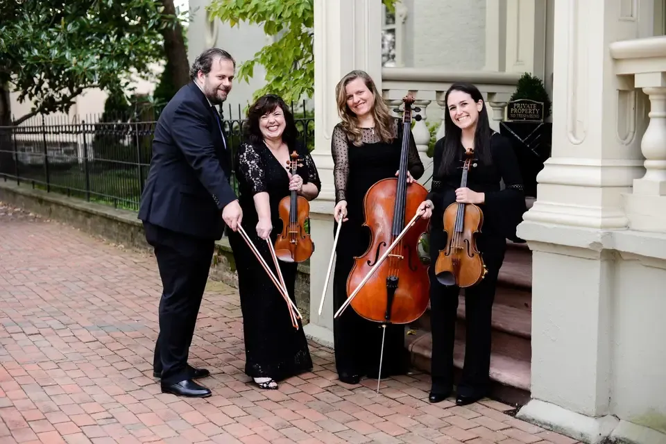 String quartet in formal black attire posing with violins and cello outdoors