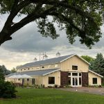 Cream-colored barn venue with cupolas and sliding doors under dramatic Nebraska sky