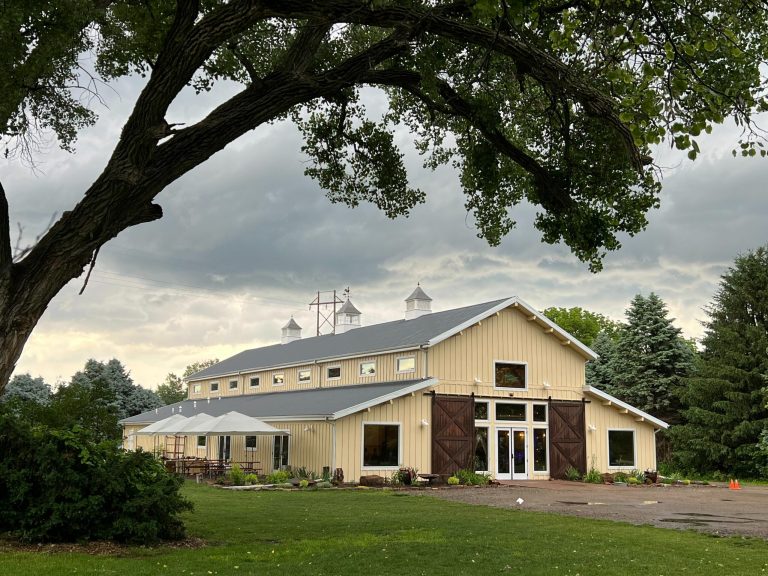 Cream-colored barn venue with cupolas and sliding doors under dramatic Nebraska sky