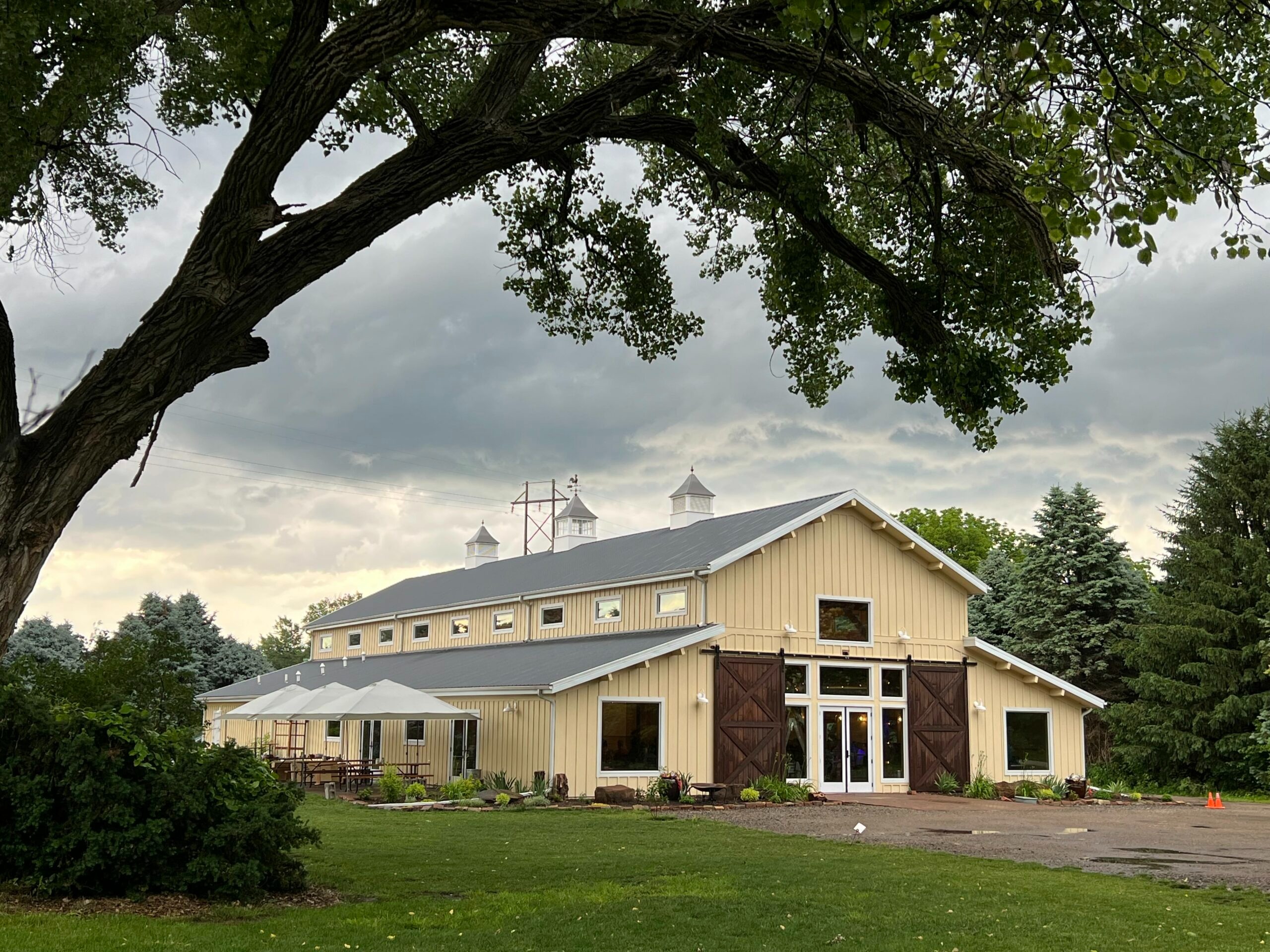 Cream-colored barn venue with cupolas and sliding doors under dramatic Nebraska sky
