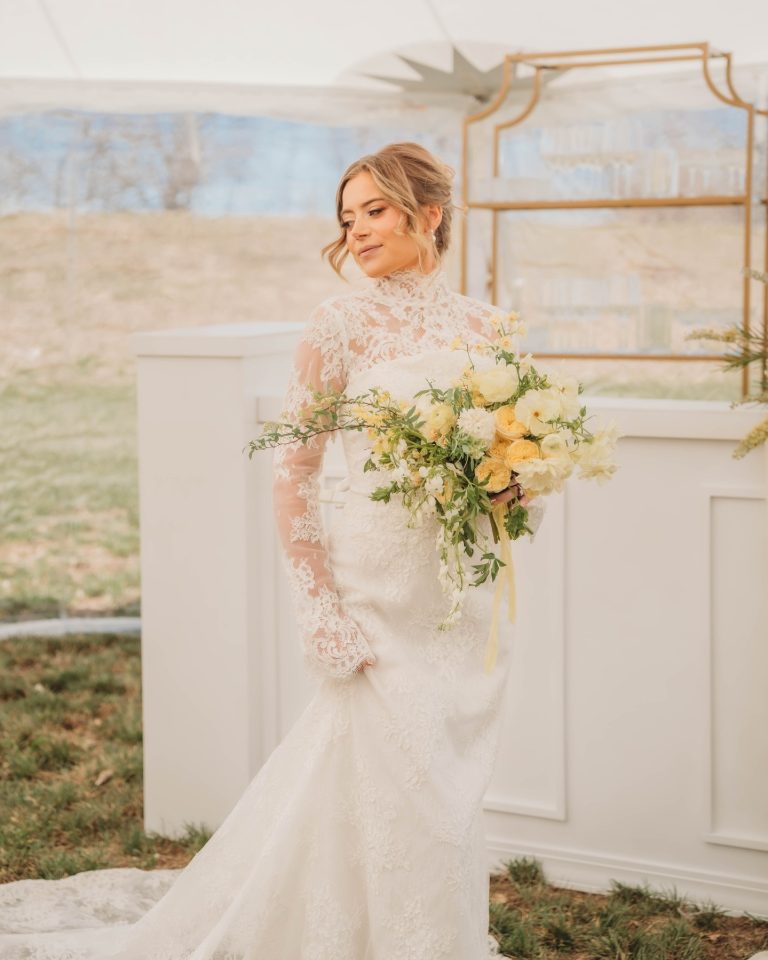 Bride in lace wedding gown holding yellow and white bridal bouquet at outdoor Nebraska ceremony