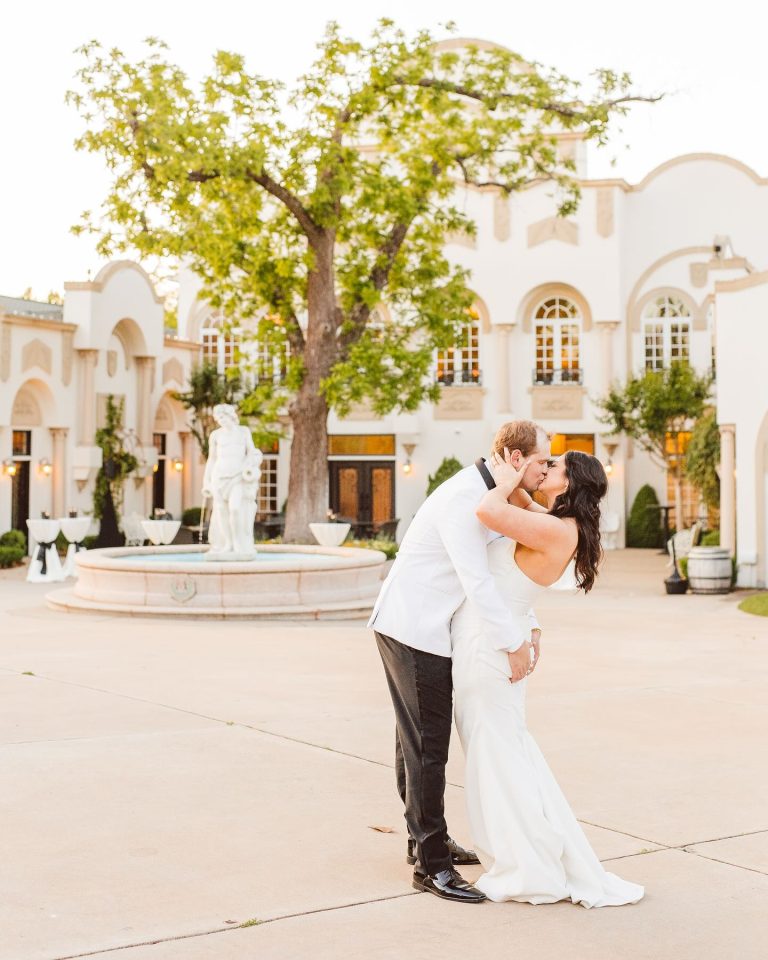 Newlywed couple dancing in front of Mediterranean-style estate with fountain