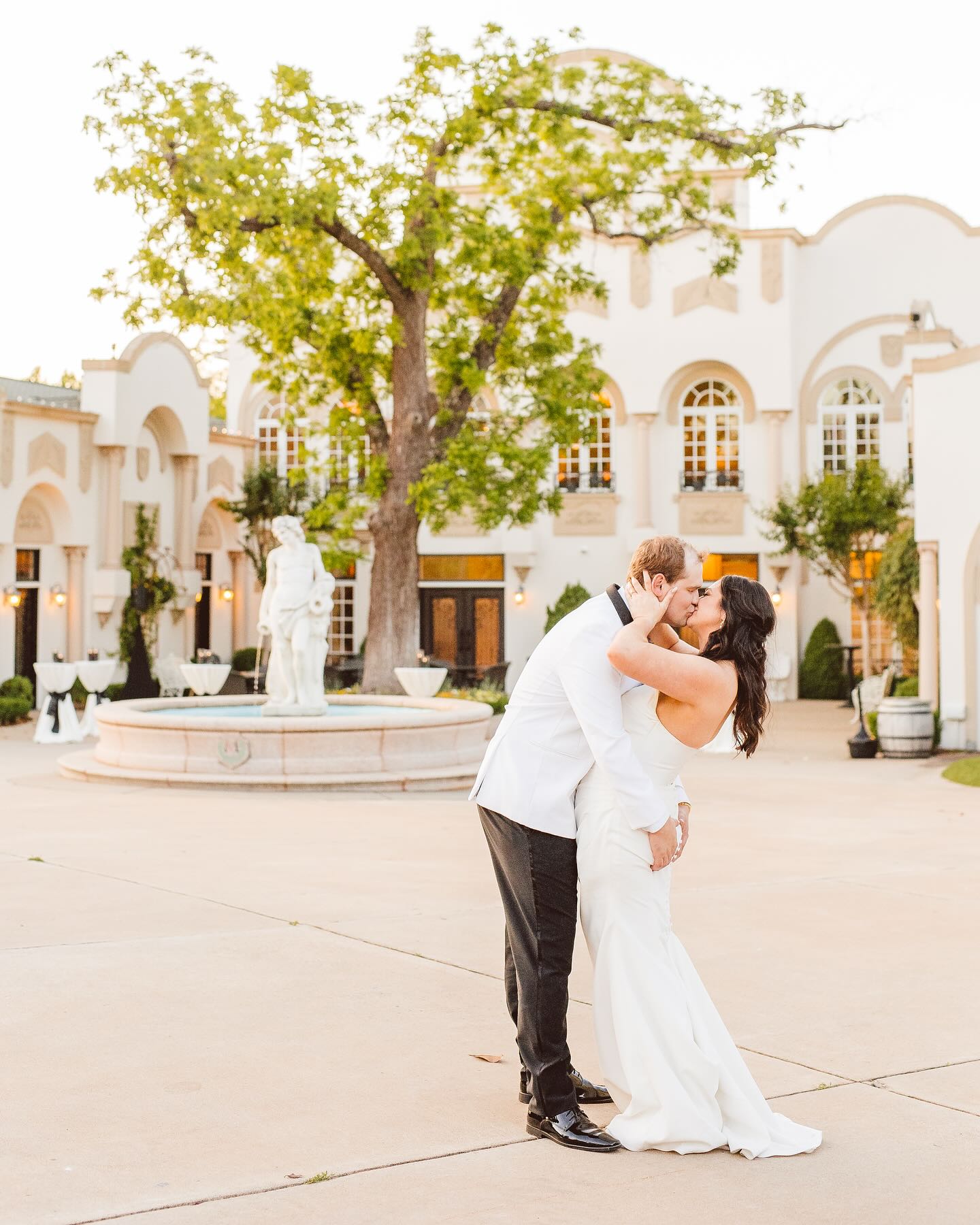 Newlywed couple dancing in front of Mediterranean-style estate with fountain