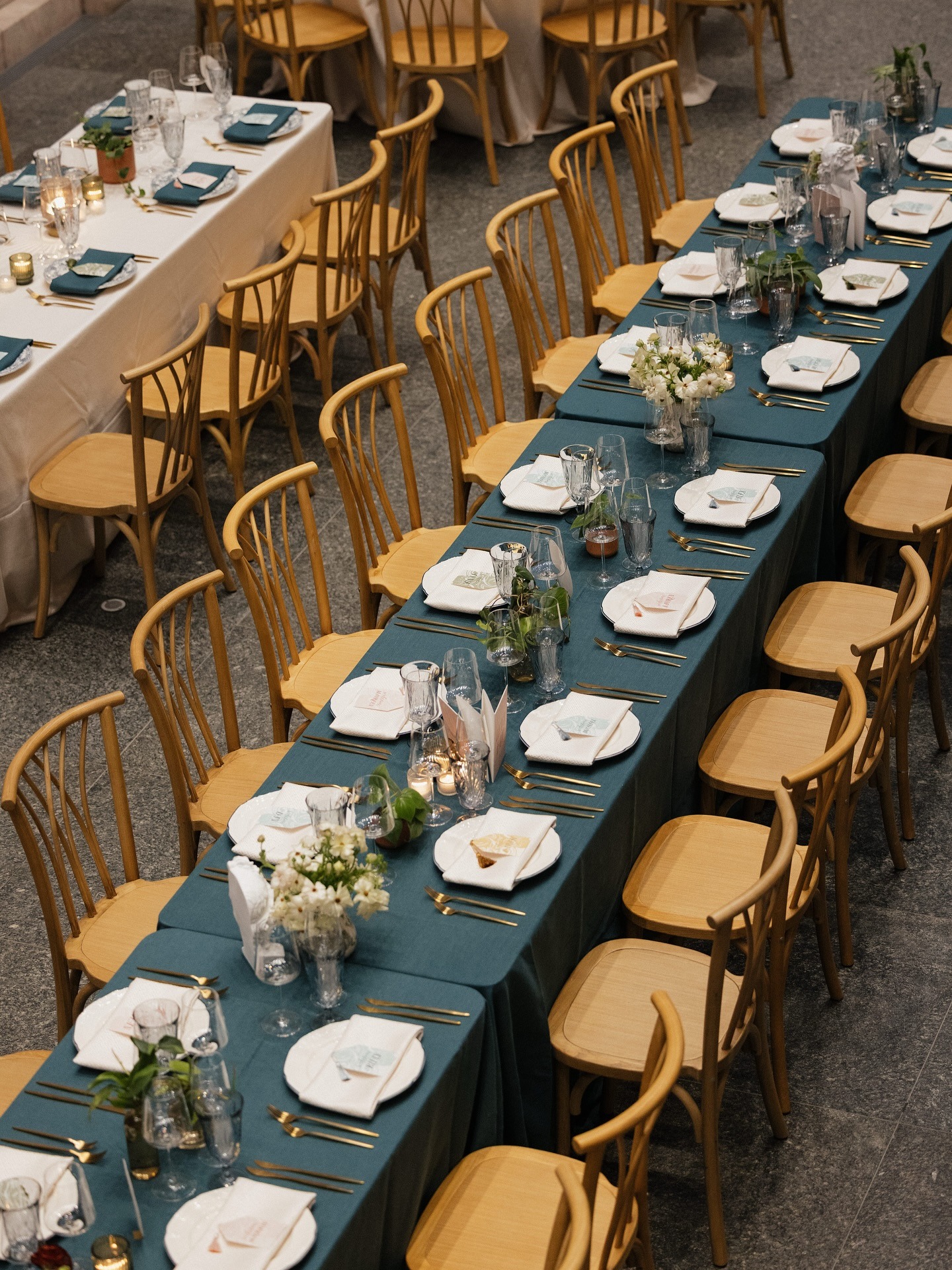 Long banquet tables with teal linens, natural wood chairs, white place settings and gold flatware at The Joslyn