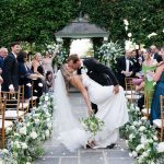 Groom dips bride for kiss during recessional as guests toss petals at ivy-covered gazebo ceremony