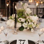 Wedding reception table with white floral centerpiece, tall candles, black place settings, and elegant place cards