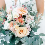 Bride holding romantic bouquet of peach, cream, and pink roses with abundant eucalyptus