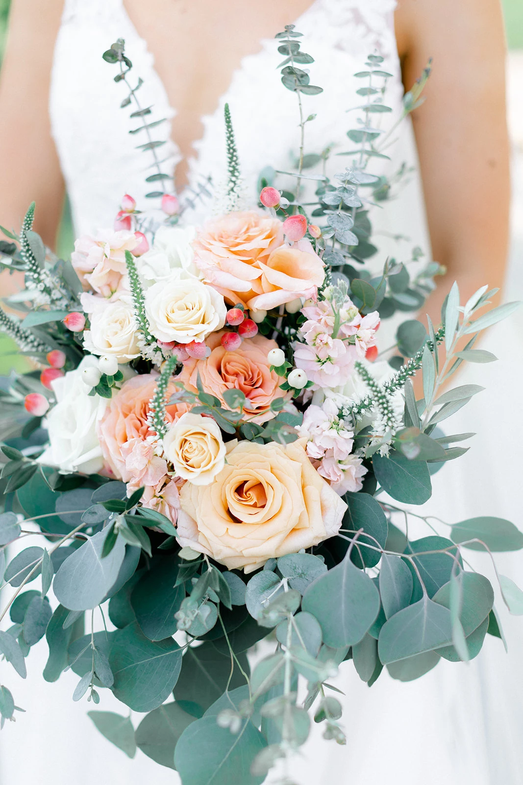 Bride holding romantic bouquet of peach, cream, and pink roses with abundant eucalyptus