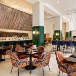 Magnolia Omaha hotel lobby bar with illuminated shelving, velvet seating, and high-top tables