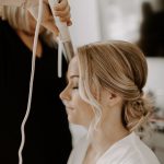 Hairstylist creating romantic updo with loose tendrils for wedding day styling