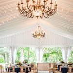 Elegant white draped tent with ornate gold chandeliers and navy and blush reception tables with gold chiavari chairs