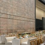 Reception tables with gold chiavari chairs set beneath modern stone architecture at The Joslyn
