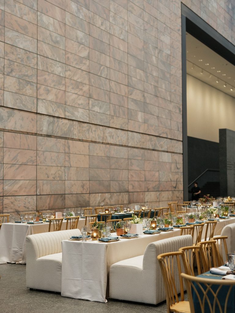 Reception tables with gold chiavari chairs set beneath modern stone architecture at The Joslyn