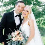 Smiling bride and groom holding peach and eucalyptus bouquet in outdoor garden setting