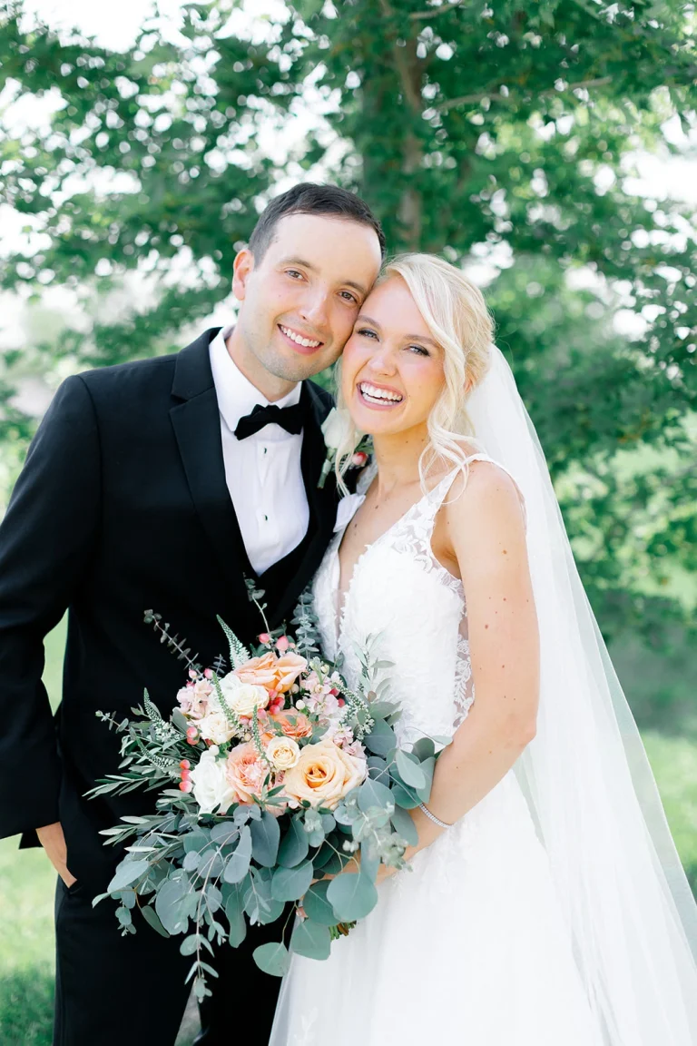 Smiling bride and groom holding peach and eucalyptus bouquet in outdoor garden setting
