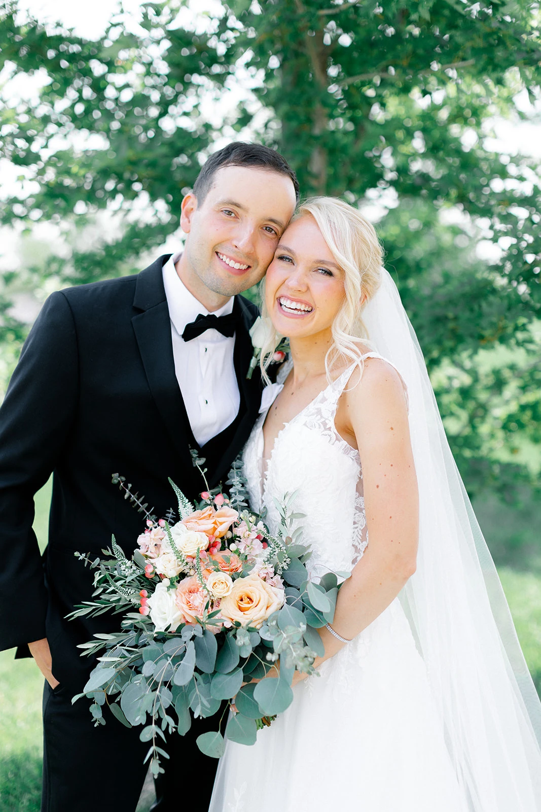 Smiling bride and groom holding peach and eucalyptus bouquet in outdoor garden setting