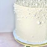 Elegant ivory wedding cake adorned with cascading pearl decorations on gold cake stand